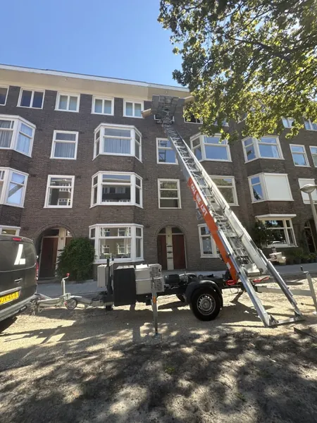 Verhuislifthuren.nl-aanhangerlift achter zwarte bus, ladder tot de dakrand van bakstenen flat. Familiebedrijf dat eerlijk zaken doet tegen een vaste prijs.