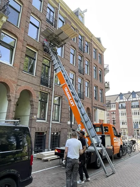 Ladderlift op Verhuislifthuren.nl-vrachtwagen naar bovenste etage van bakstenen pand. Een appje, en je verhuislift in de regio is geregeld.