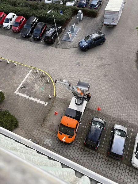 Van bovenaf gezien: Verhuislifthuren.nl-vrachtwagen met ladderlift omhoog op een parkeerplaats. Een appje, en je verhuislift in de regio is geregeld.