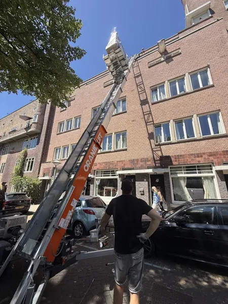 Rode bakstenen flat met aanhangerlift naar de bovenste etage, verhuizer bij bediening. Bij Verhuislifthuren.nl huur je een verhuislift altijd met operator.