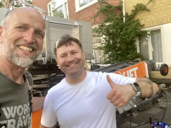 Twee lachende mannen op een selfie bij de Verhuislifthuren.nl-aanhangerlift voor een huis. Piano of Amerikaanse koelkast, wij tillen het veilig omhoog.