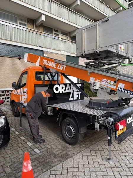 Verhuizer bij de zijkast van de Verhuislifthuren.nl-vrachtwagen voor een flat met balkons. Onze ladderlift hijst zware kasten zo de hoogte in.