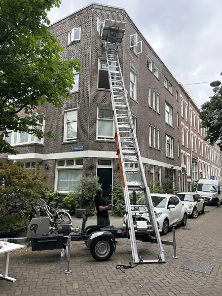 Donker bakstenen hoekpand met aanhangerlift, ladder naar de bovenste etage, bewolkt. Vandaag gebeld, morgen staat Verhuislifthuren.nl al voor je deur.