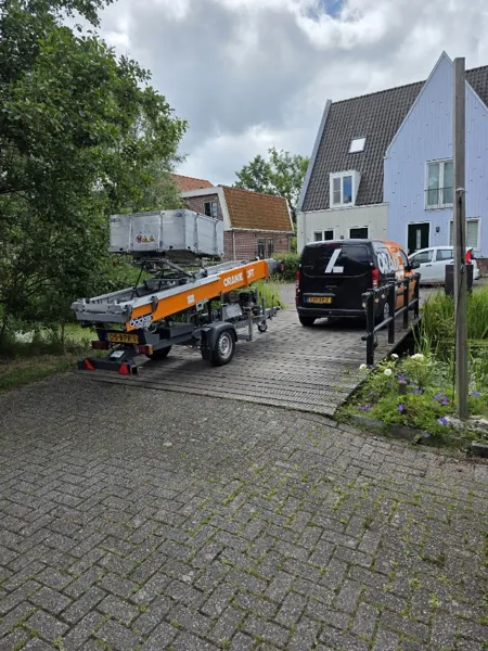 Aanhangerlift en zwarte Verhuislifthuren.nl-bus op houten brug bij houten woning met puntgevel. Piano of Amerikaanse koelkast, wij tillen het veilig omhoog.