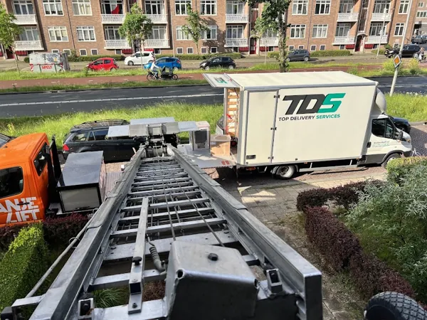 Blik omlaag langs de ladder van de Verhuislifthuren.nl-vrachtwagen naar een bakwagen met dozen. Familiebedrijf dat eerlijk zaken doet tegen een vaste prijs.