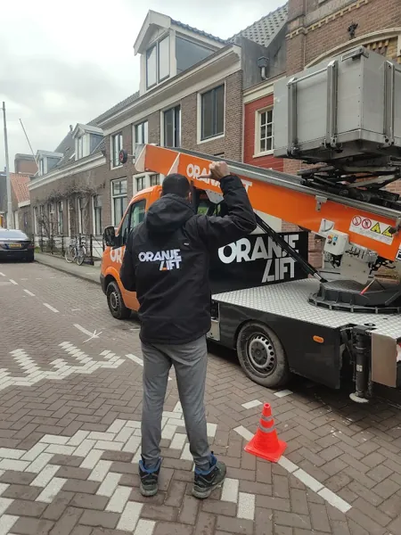 Verhuizer in Verhuislifthuren.nl-jas naast de vrachtwagen met ladderlift in ruststand, bewolkt. Piano of Amerikaanse koelkast, wij tillen het veilig omhoog.
