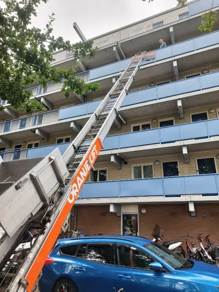 Verhuislifthuren.nl-ladder omhoog naar bovenste galerij van een flat met blauwe balkonhekken. Een appje, en je verhuislift in de regio is geregeld.