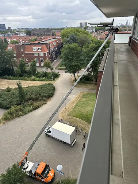 Vanaf een hoge galerij gezien reikt de ladder van de Verhuislifthuren.nl-vrachtwagen tot boven. Onze ladderlift hijst zware kasten zo de hoogte in.