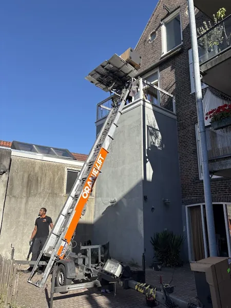 In een achtertuin staat de Verhuislifthuren.nl-aanhangerlift met de ladder naar een dakterras. Een appje, en je verhuislift in de regio is geregeld.