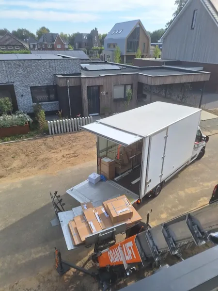 Dozen op het Verhuislifthuren.nl-platform bij een open bakwagen in nieuwbouwwijk, van bovenaf. Voor een smalle straat sturen we de stille aanhangerlift.