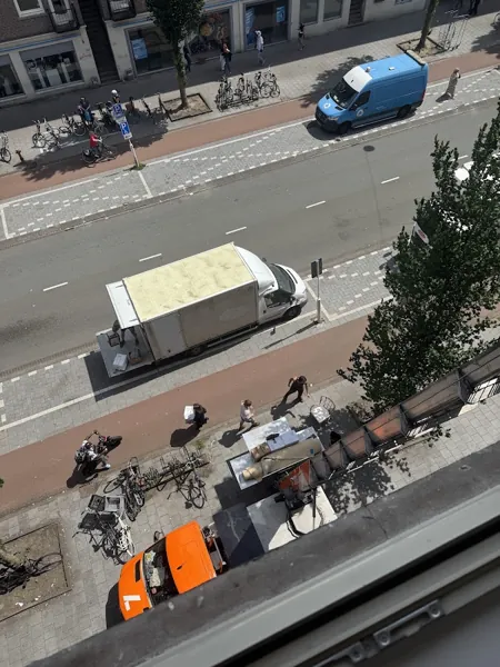 Vanuit een raam: Verhuislifthuren.nl-vrachtwagen en verhuizers op een drukke winkelstraat. Familiebedrijf dat eerlijk zaken doet tegen een vaste prijs.