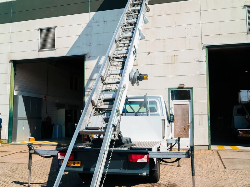 Witte verhuislift met uitgeschoven ladder bij een loods